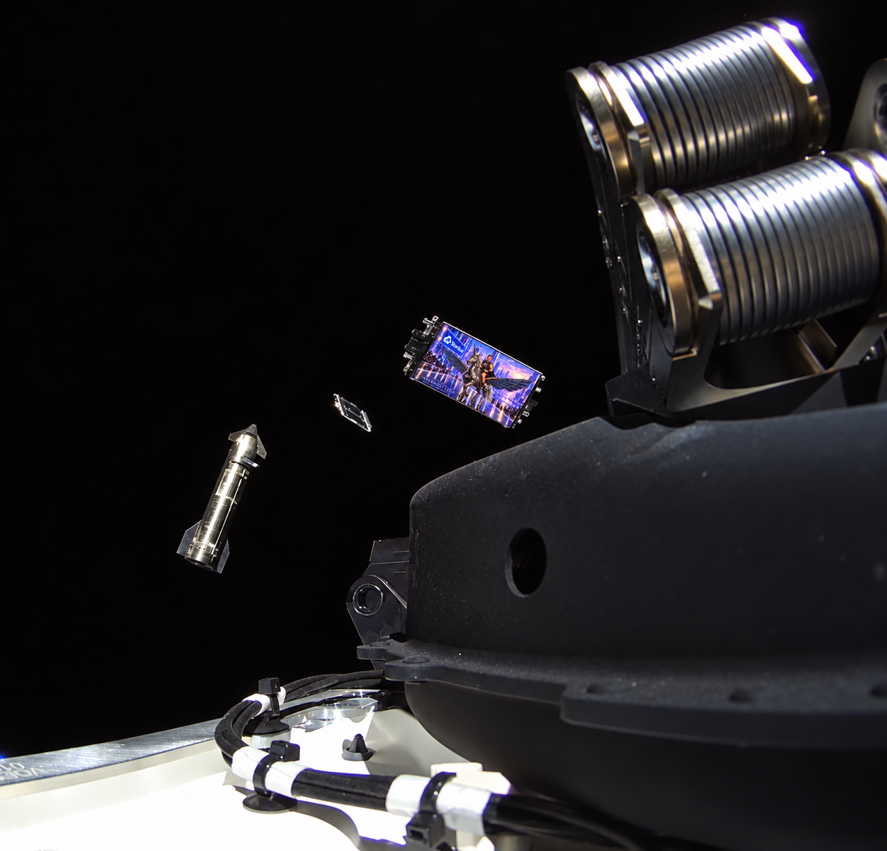Satellite hardware fills the foreground against black space. A small violet-and-blue image of Philip Johnston’s unicorn runway portrait is inserted on a tilted satellite surface, with a silver spacecraft in the distance.